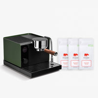 A sleek espresso machine in dark green and black with a chrome portafilter and wooden handle, shown alongside three white coffee bean bags labeled 'Koe Die Hopper Roasted Coffee' on a clean white background.