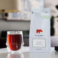 Lifestyle shot of a Kiss the Hippo Low Caf coffee bag with a cup of brewed coffee