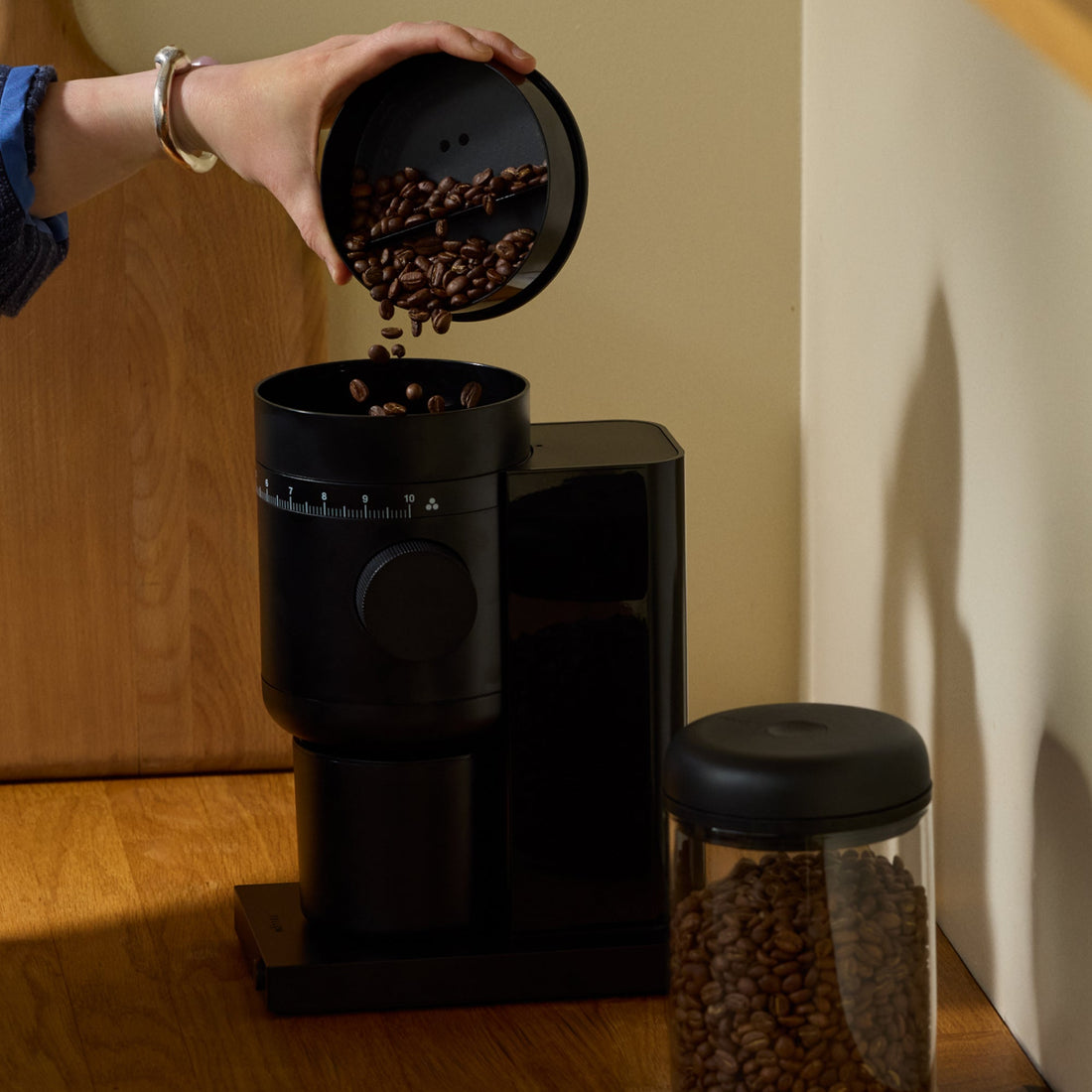 Coffee beans being poured into a Fellow Opus 2 grinder on a kitchen worktop