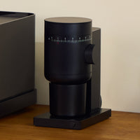 Fellow Opus 2 conical burr grinder in matte black on a wooden worktop beside its box