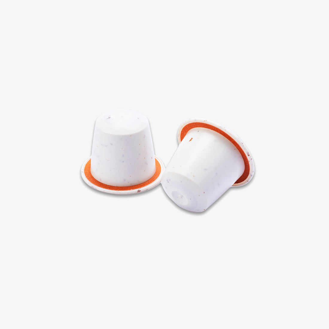 Two white coffee capsules with orange rims, one standing upright and the other lying on its side, shown on a light grey background.